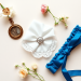A flat lay of wedding items: a vintage locket, a modern engagement ring, a delicate handkerchief, and a blue garter, arranged on a soft floral back...
