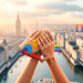 Colorful abstract 3D illustration of rainbow shapes and intertwined hands symbolizing LGBTQ+ unity, set against a softly lit UK cityscape background.